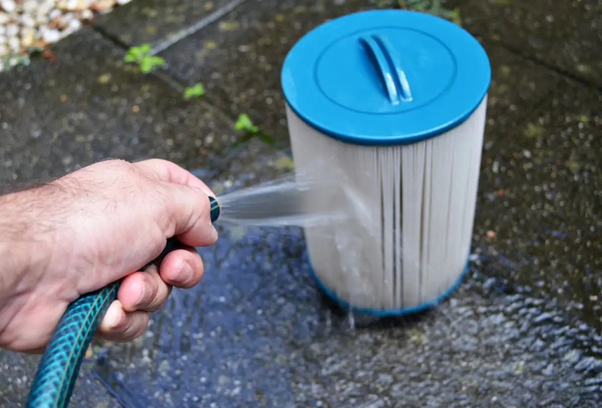 Spraying out the hot tub filter with a hose - How Much Does a Hot Tub Cost to Run